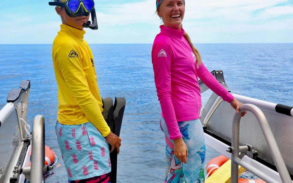 Snorkelkujący w maskach i płetwach w wodzie obok rufowej platformy łodzi rafowej zacumowanej na Great Barrier Reef