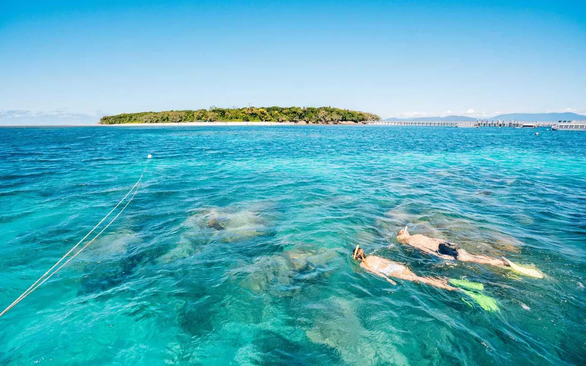 Ein weißer Sandstrand und flaches türkisfarbenes Wasser auf einer tropischen Insel vor Queensland